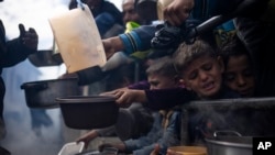 FILE - Palestinians line up for a meal in Rafah, Gaza Strip, Feb. 16, 2024. The World Food Program said Tuesday it has paused deliveries of food to isolated northern Gaza because of chaos across the territory, hiking fears of potential starvation.