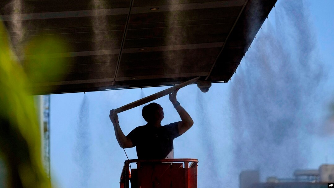 Un hombre trabaja afuera bajo los rociadores, el jueves 13 de julio de 2023 en el centro de Phoenix, Arizona, que está siendo azotado con temperaturas de más de 40 grados Celsius y advertencias de calor excesivo. (Foto AP/Matt York)