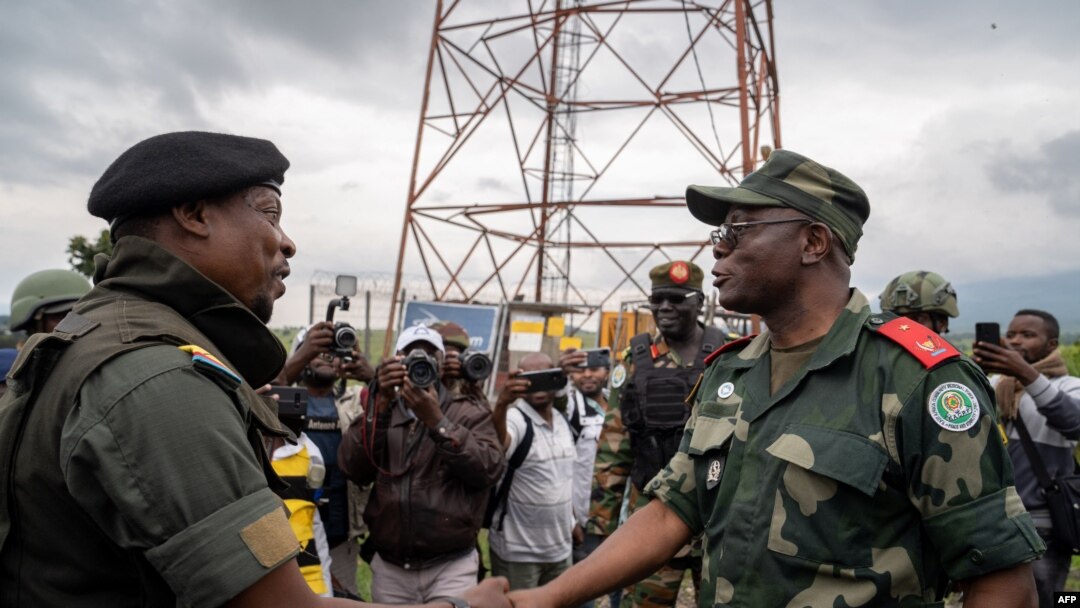 Naibu kamanda wa kikosi cha kikanda cha Afrika Mashariki (EACRF) Brigedia Jenerali Emmanuel Kaputa (Kulia) akiwa na msemaji wa kundi la waasi la M23 Willy Ngoma (kushoto) wakipeana mikono huko Kibumba DRC, Desemba 23, 2022. Picha na GLODY MURHABAZI/AFP.
