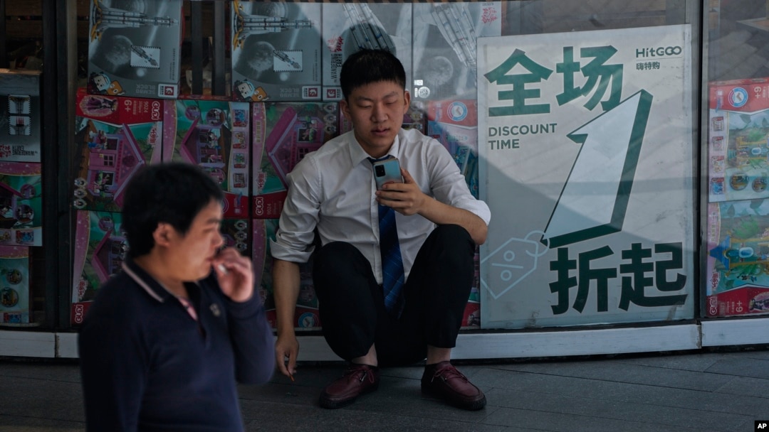 一名男子坐在北京一棟商業大樓張貼的折扣廣告前。 (2024年5月27日)