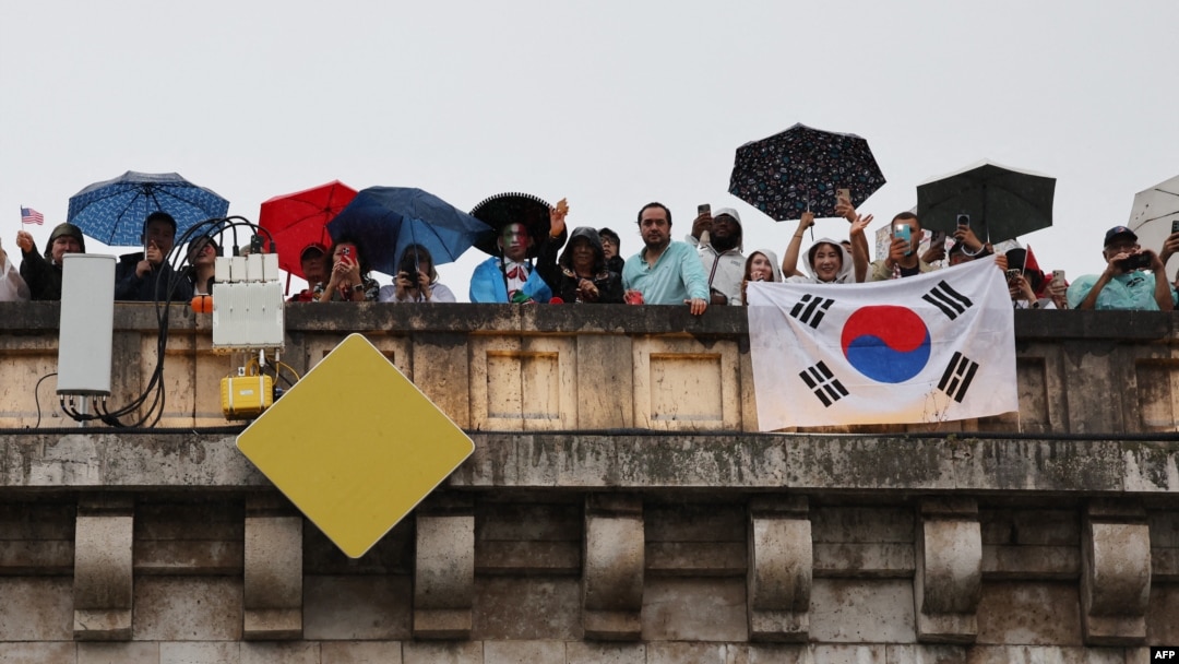 Spectators with a flag of South Korea look on from a Paris bridge to watch the floating parade on the river Seine during the Olympic Games opening ceremony, July 26, 2024.