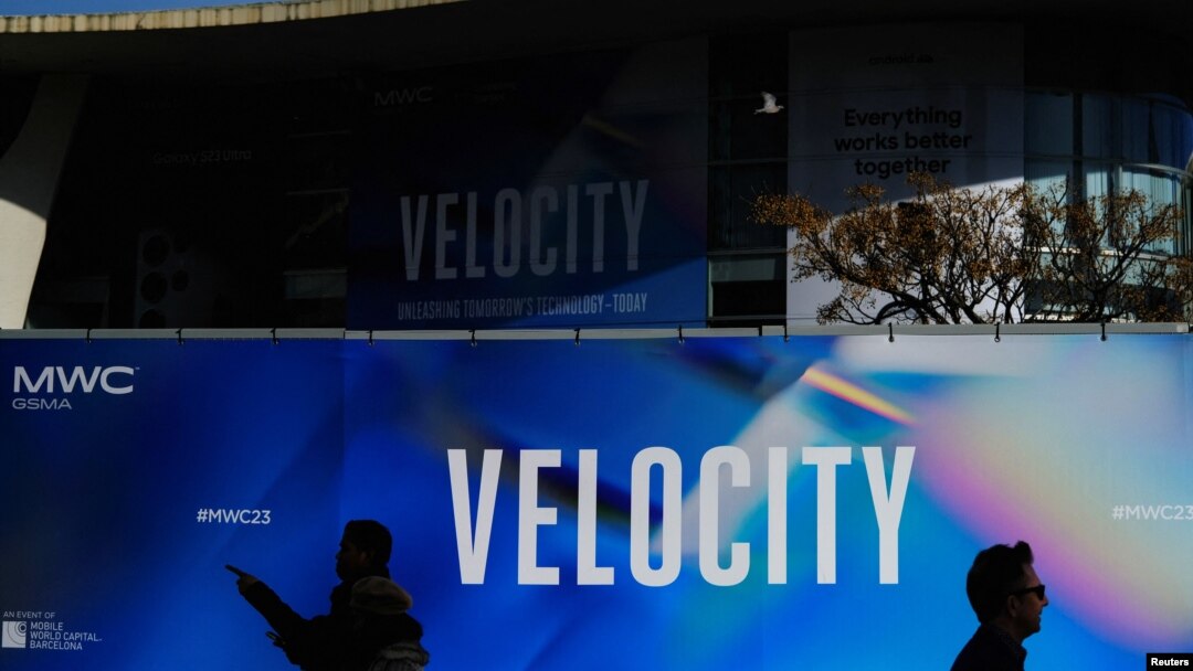 Workers walk past a billboard of GSMA's 2023 ahead of the Mobile World Congress in Barcelona, Spain, Feb. 25, 2023.