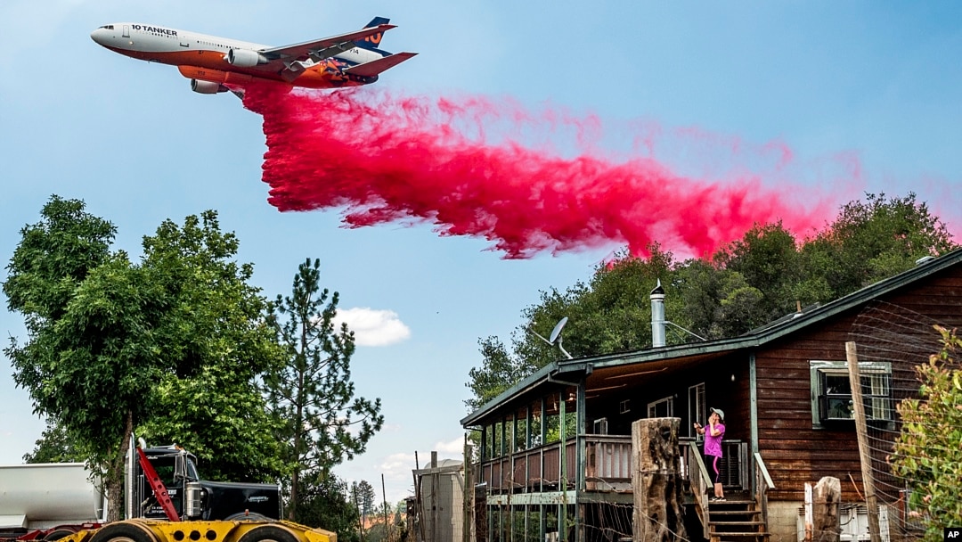 FILE - A woman watches an air tanker drop retardant as the Electra Fire burns towards her home in Amador County, California, on July 5, 2022. 