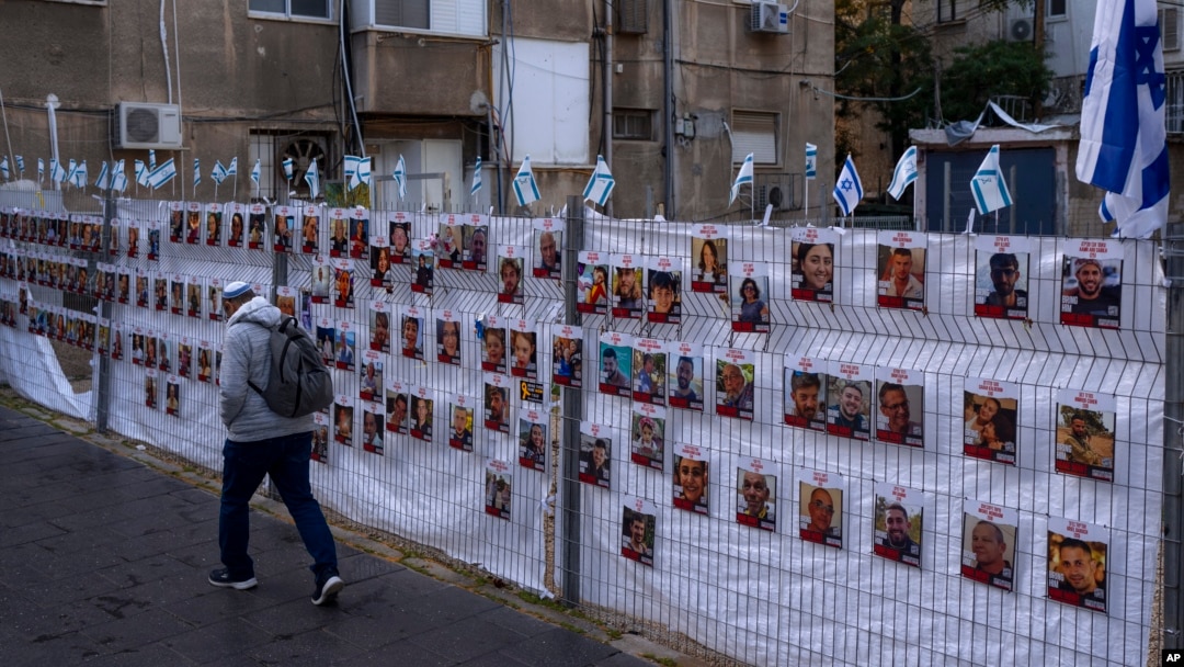 A man passes by a fence with photographs of hostages, mostly Israeli civilians who were abducted during the Oct. 7, unprecedented Hamas attack on Israel, in Ramat Gan, Israel, Nov. 22, 2023.