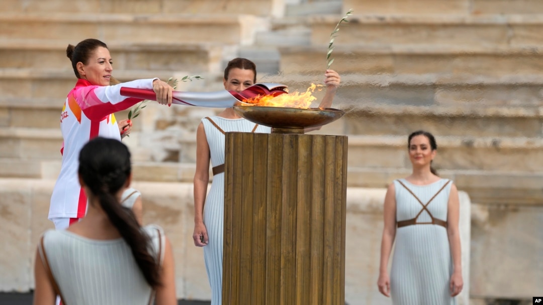 La campeona griega de esquí Paraskevi Ladopoulou (izquierda) enciende la antorcha durante la ceremonia de entrega de la llama olímpica, en el estadio Panathinean, en Atenas, Grecia, el 19 de octubre de 2021.
