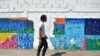 El artista venezolano Oscar Olivares pasa junto a un colorido mural ecológico que está creando con tapas de botellas para crear conciencia sobre el reciclaje, en Caracas, Venezuela, 19 de agosto de 2022. REUTERS/Gaby Oraa 