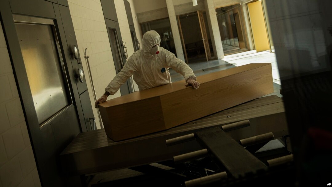 FILE - A worker, wearing full protective gear, moves the casket of a victim of COVID-19 to be cremated during a partial lockdown to prevent the spread of coronavirus at the Pontes crematorium center in Lommel, Belgium, Thursday, April 16, 2020. (AP Photo/Francisco Seco, File)
