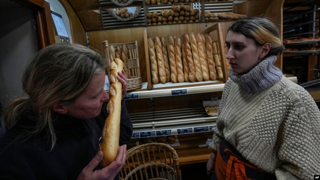 Bakery owner Florence Poirier, left, smells a fresh baguette as Mylene Poirier stands next to her at a bakery, in Versailles, France, Nov. 29, 2022. The humble baguette is being added to the U.N.'s list of intangible cultural heritage.