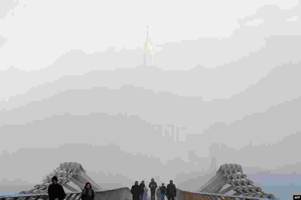 Pedestrians cross the Millennium Footbridge in front of London's St. Paul's Cathedral, shrouded in fog.