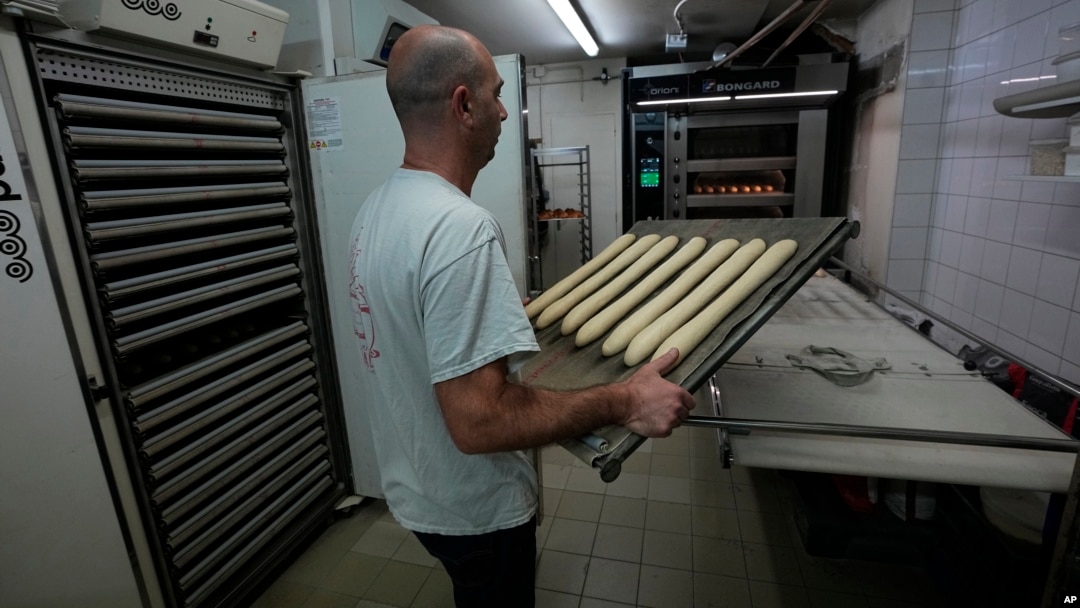 Baker David Buelens carries uncooked baguettes to the oven at a bakery in Versailles, west of Paris, Nov. 29, 2022.