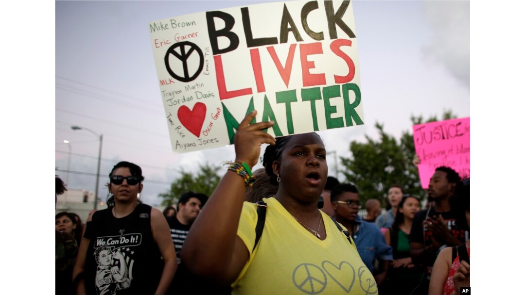 FILE - Desiree Griffiths holds up a sign saying "Black Lives Matter," with the names of Michael Brown and Eric Garner, two black men killed by police, during a protest in Miami, Florida, Dec. 5, 2014.