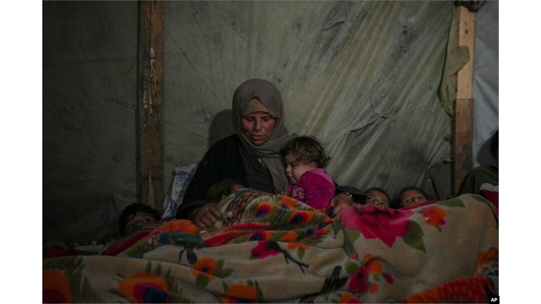 Reda Abu Zarada wraps herself and her grandchildren in blankets as they prepare to sleep in their tent at a camp in Khan Younis, Gaza Strip, Dec. 19, 2024.