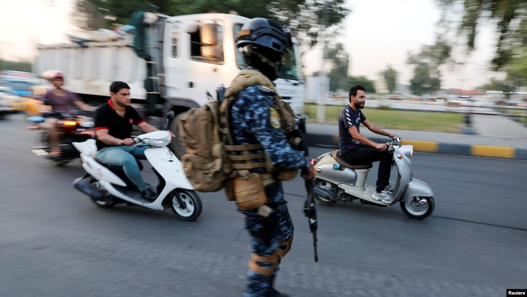 Men ride motorbikes past a member of Iraqi federal police in a street in Baghdad, Iraq October 7, 2019. 