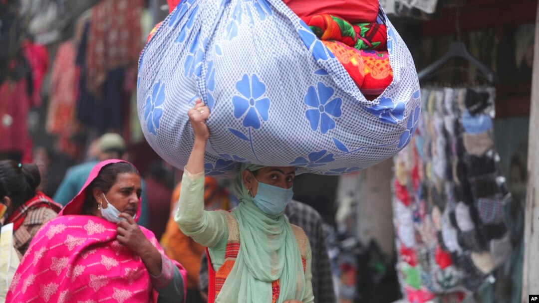 A woman wearing a face mask as a precaution against the coronavirus carries a load of blankets at a market in Jammu, India, Jan. 21, 2022.