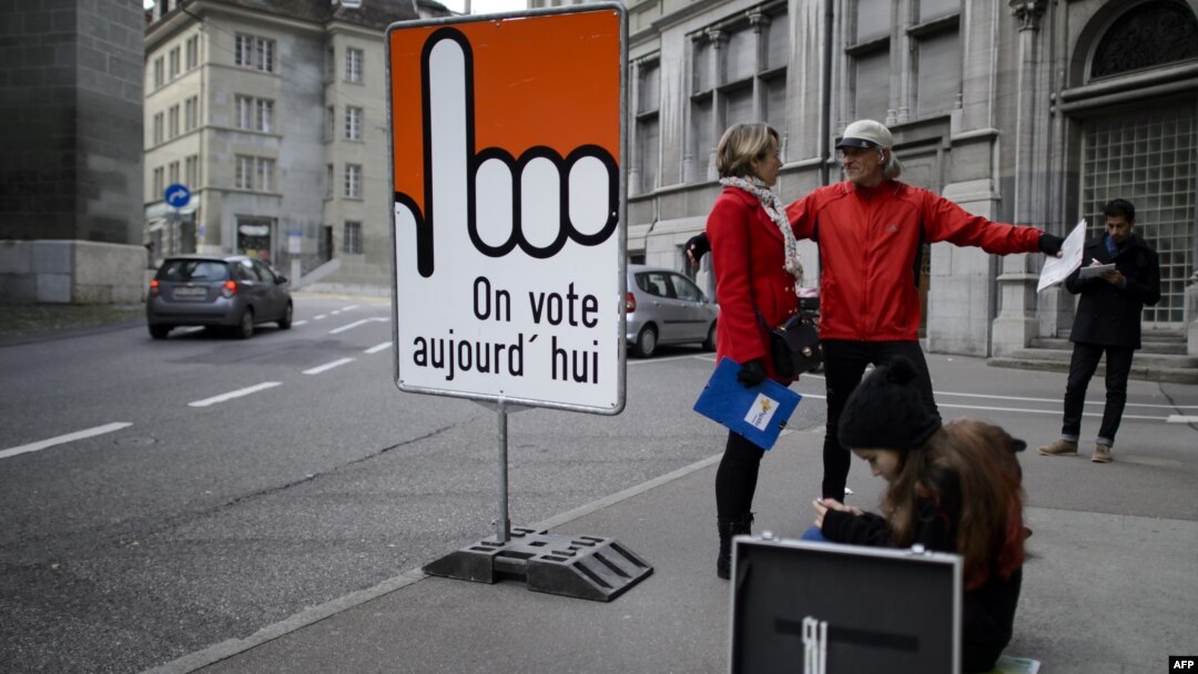 People stand next to a board reading in French "We vote today" in the old town section of Fribourg, Switzerland, Nov. 30, 2014. 