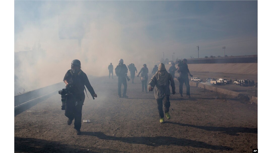 Migrants run from tear gas launched by U.S. agents, amid photojournalists covering the Mexico-U.S. border, after a group of migrants got past Mexican police at the Chaparral crossing in Tijuana, Nov. 25, 2018.