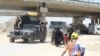 Families take shelter under a bridge where they meet trucks and buses transporting civilians to camps while soldiers travel the opposite direction to the front lines in Mosul, Iraq, June 4, 2017. (H. Murdock/VOA)