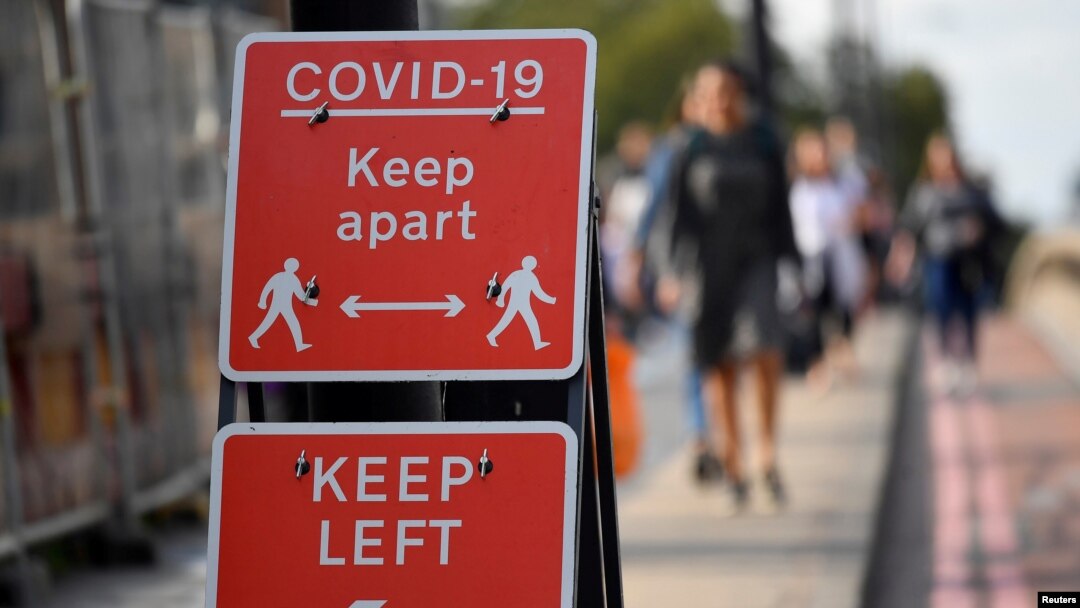 FILE - Pedestrians walk near public health signs in London, Britain, Sept. 11, 2020. 