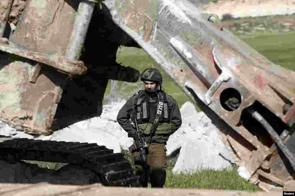 An Israeli soldier stands guard during the demolition of a Palestinian house at the order of the Israeli army, in the West Bank town of Dura, south of Hebron. The owners of the house said they were informed by the Israeli army that the demolition was carried out because they did not have an Israeli-issued construction permit.