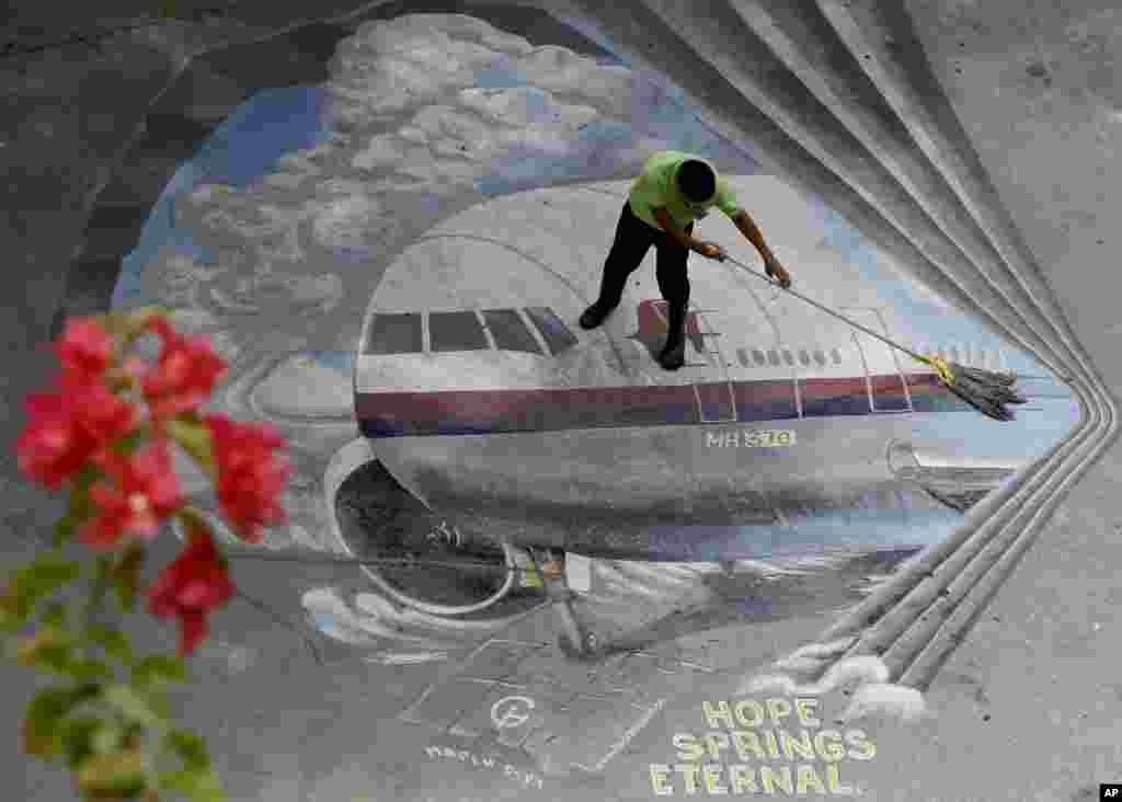 A school utility worker mops a mural depicting the missing Malaysia Airlines Flight 370 at the Benigno "Ninoy" Aquino High School campus at Makati city east of Manila, Philippines.
