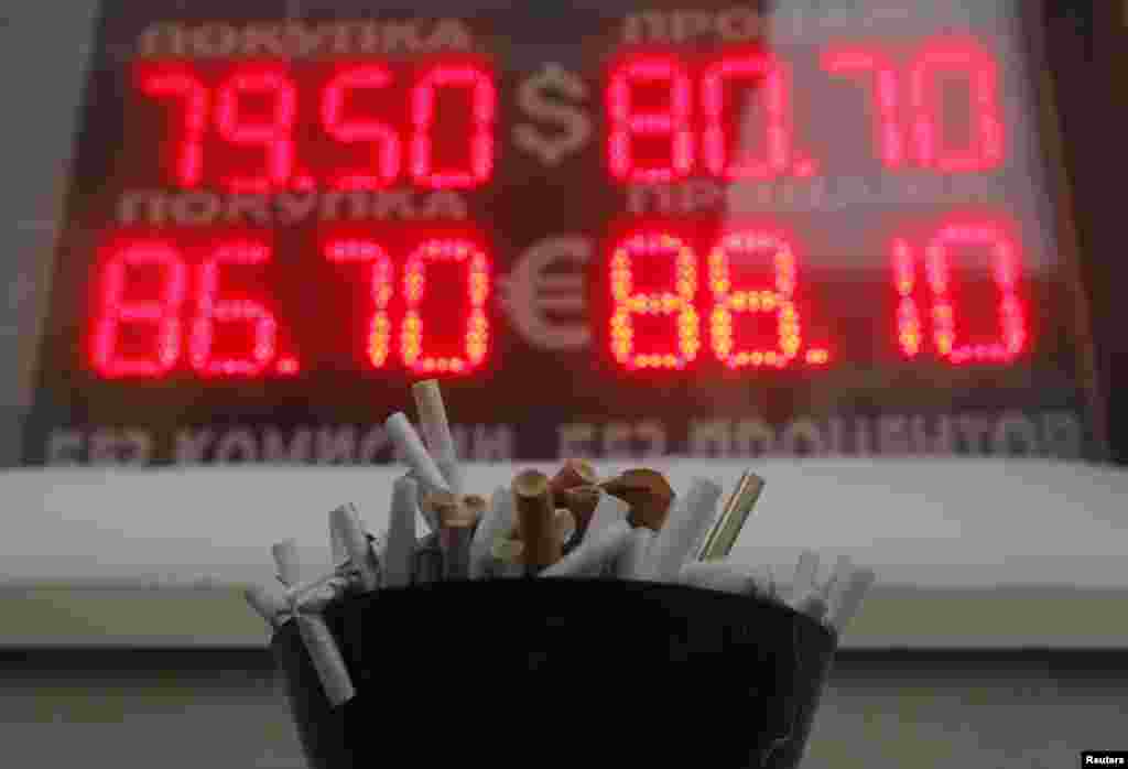 An ashtray filled with cigarette butts in front of a board showing currency exchange rates of the U.S. dollar and euro against the ruble in Moscow, Russia. The Russian ruble weakened to a new record low against the dollar on Wednesday as the mood on global markets was torrid and oil prices slumped. 