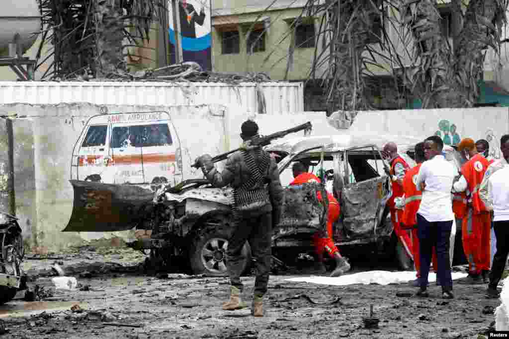 A police officer keeps watch as Red Crescent workers remove the body of a victim at the scene of a suicide car bomb explosion near the president's residence, in Mogadishu, Somalia, Sept. 25, 2021.