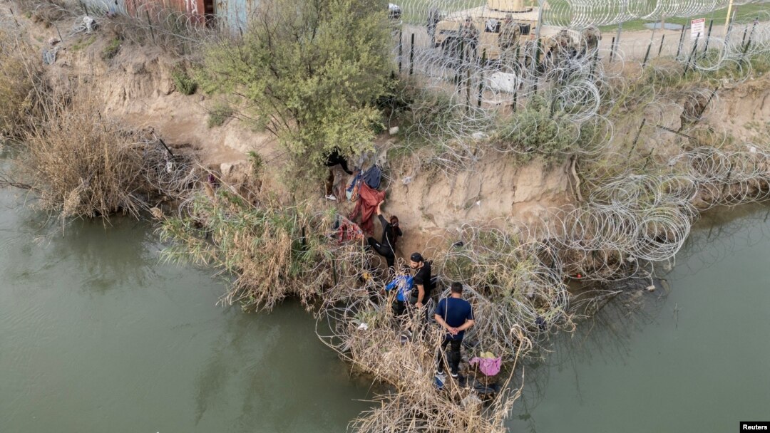 Un grupo de migrantes intenta atravesar una valla de alambre a orillas del río Grande mientras miembros de la Guardia Nacional de EEUU hacen guardia al otro lado de la valla en Eagle Pass, Texas, Estados Unidos, el 27 de febrero de 2024.