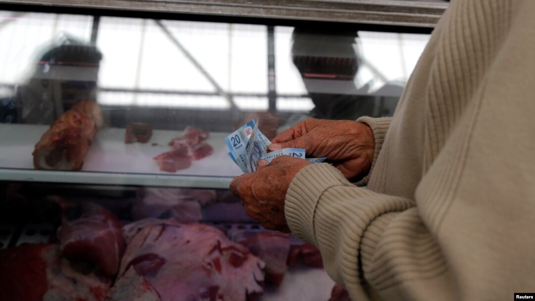 FILE - A man counts money to pay for goods at the Granada market in Mexico City, Jan. 10, 2017. 