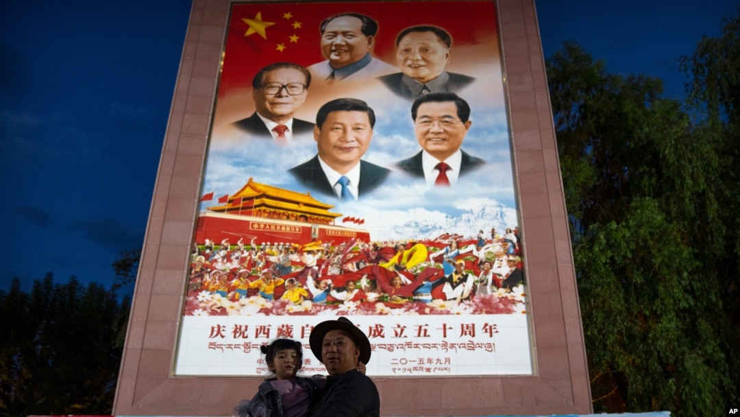 FILE - A man holds a girl in front of a large mural depicting Chinese President Xi Jinping and other Chinese leaders at a public square at the base of the Potala Palace in Lhasa in western China's Tibet Autonomous Region, June 1, 2021.