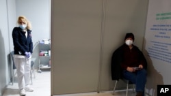 A nurse stands inside a vaccination point as a man waiting to get a dose of Moderna COVID-19 vaccine, sits at the vaccination mega center in Athens, Feb. 15, 2021.