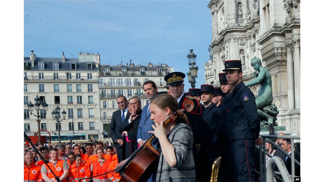French Interior Minister Christophe Castaner, third left, and other officials listen to cello player Armance Quero during a ceremony in front of the Paris city hall, April 18, 2019.