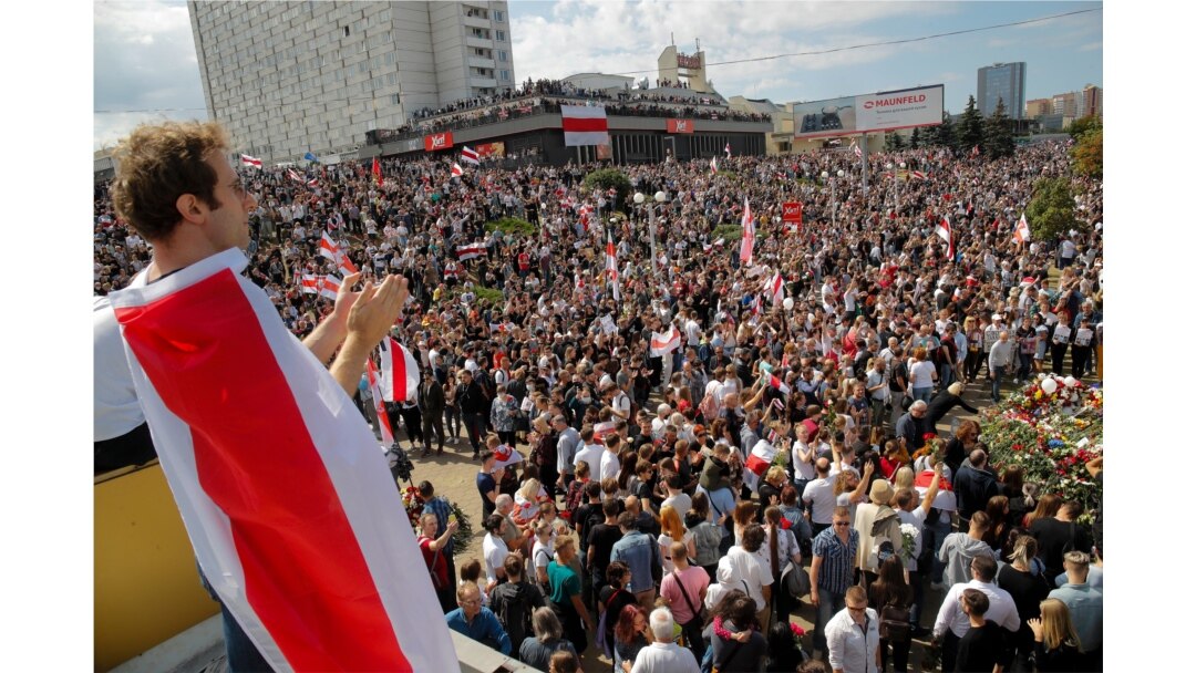 People hold old Belarusian national flags while gathered at the place where Alexander Taraikovsky died during clashes protesting election results, in Minsk, Belarus, Aug. 15, 2020.