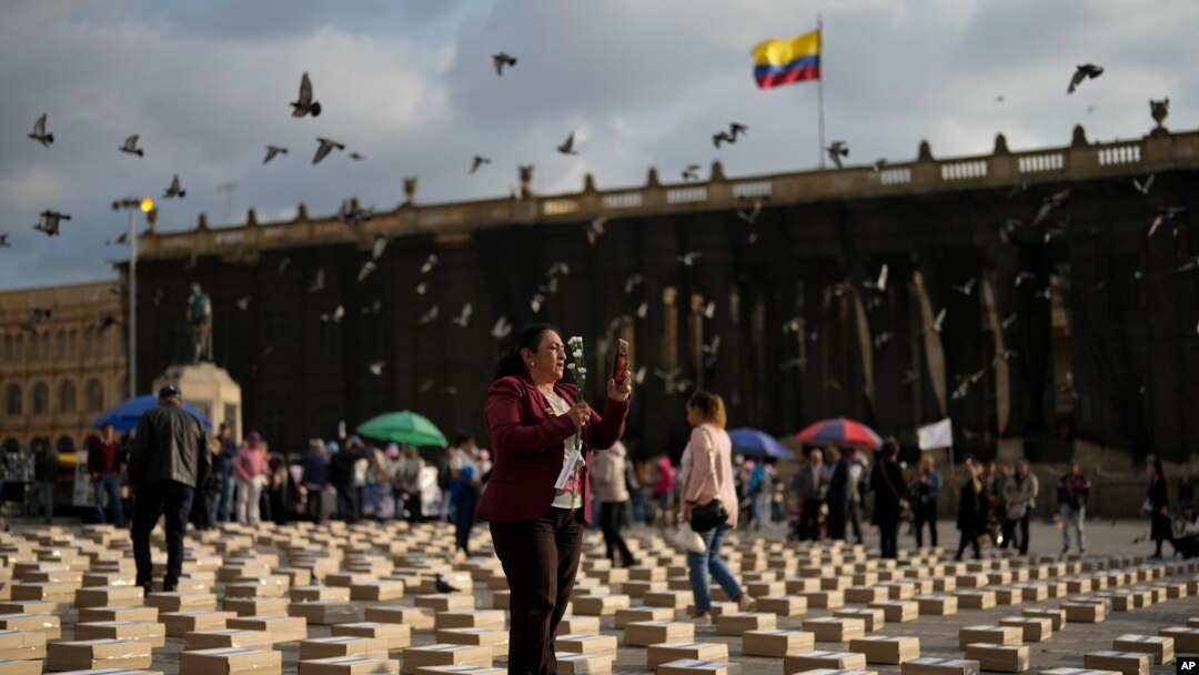Una mujer de pie entre cajas que representan féretros, mientras rinde tributo a antiguos guerrilleros y líderes sociales asesinados, desde que se firmó un acuerdo de paz en 2016 entre rebeldes de las FARC y el gobierno colombiano, el martes 20 de febrero de 2024, en Bogotá. 