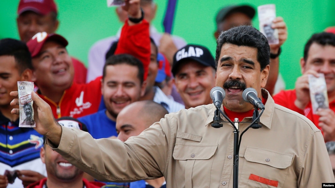 FILE - Venezuela's President Nicolas Maduro holds up a mock 100-bolivar bill depicting the president of the National Assembly Henry Ramos Allup, during a pro-government rally in Caracas, Venezuela, Dec. 17, 2016.