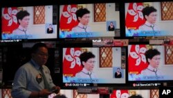 FILE - A shopper walks near televisions broadcasting Hong Kong Chief Executive Carrie Lam's speech in Hong Kong, Oct. 16, 2019.