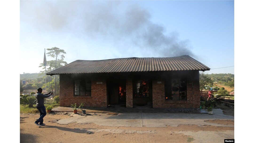 A man uses a cellphone to take pictures of a burning school office in Mashau Dolly village, in South Africa's Limpopo province, May 5, 2016.