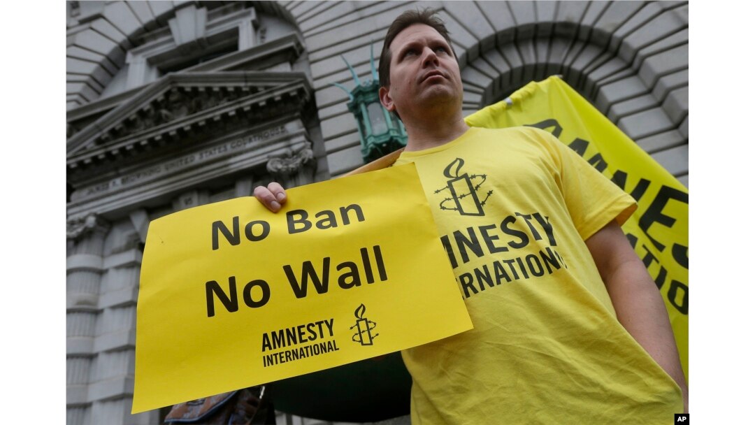 FILE - William Butkus of Amnesty International holds up a sign outside the 9th U.S. Circuit Court of Appeals in San Francisco, Feb. 7, 2017.