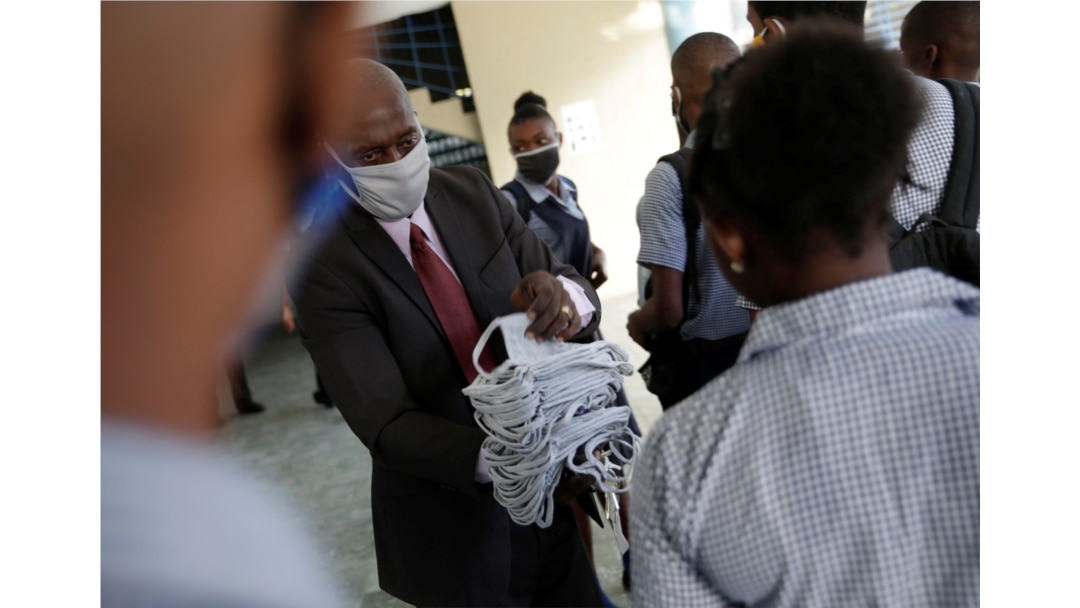 Principal Jean Marc Charles delivers face masks to pupils, to prevent the spread of the coronavirus disease, before attending to the first day of school after holidays, at Lycee National de Petion Ville, in Port au Prince, Aug. 10, 2020.
