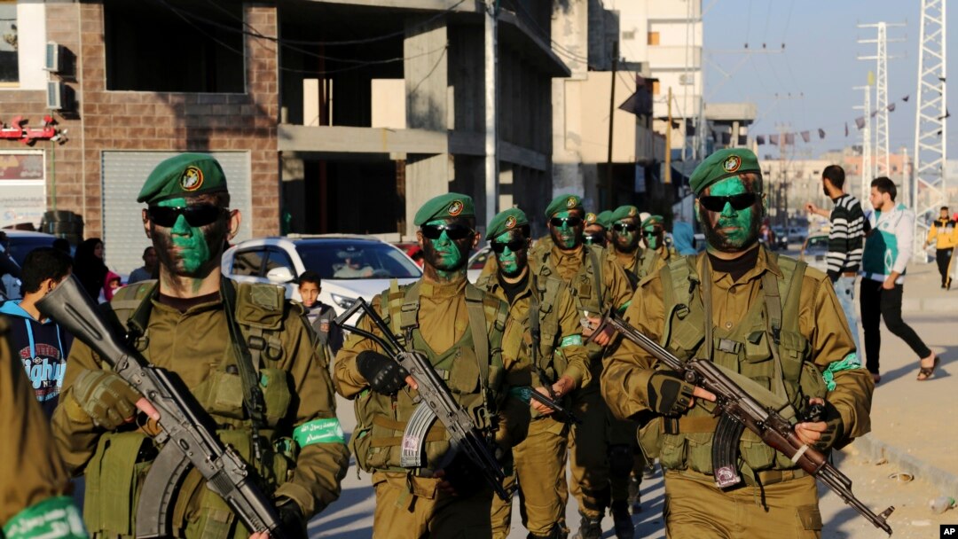 FILE - Masked militants from the Izzedine al-Qassam Brigades, a military wing of Hamas, paint their faces with green color while marching along the streets of Nusseirat refugee camp, Central Gaza Strip, Thursday, Jan. 19, 2017.
