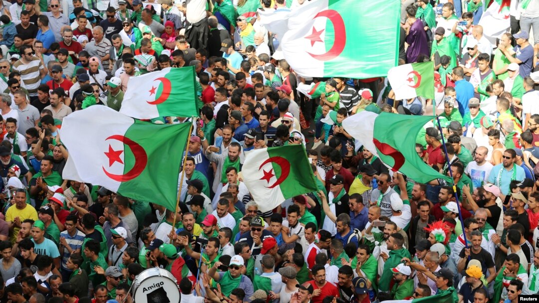 FILE - Demonstrators gesture and carry flags during a protest demanding the removal of the ruling elite and prosecution of former officials linked to former President Abdelaziz Bouteflika, in Algiers, Algeria, June 14, 2019.