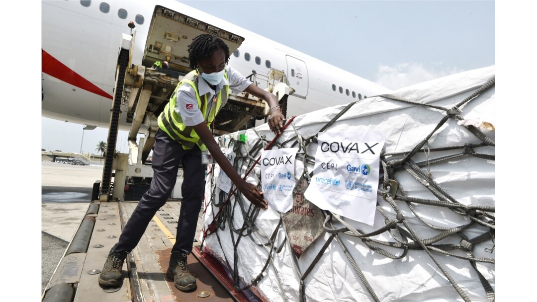 FILE - A woman attaches COVAX stickers to a shipment of AstraZeneca Covid-19 vaccine from a plane at Felix Houphouet Boigny airport of Abidjan on Feb. 26, 2021.