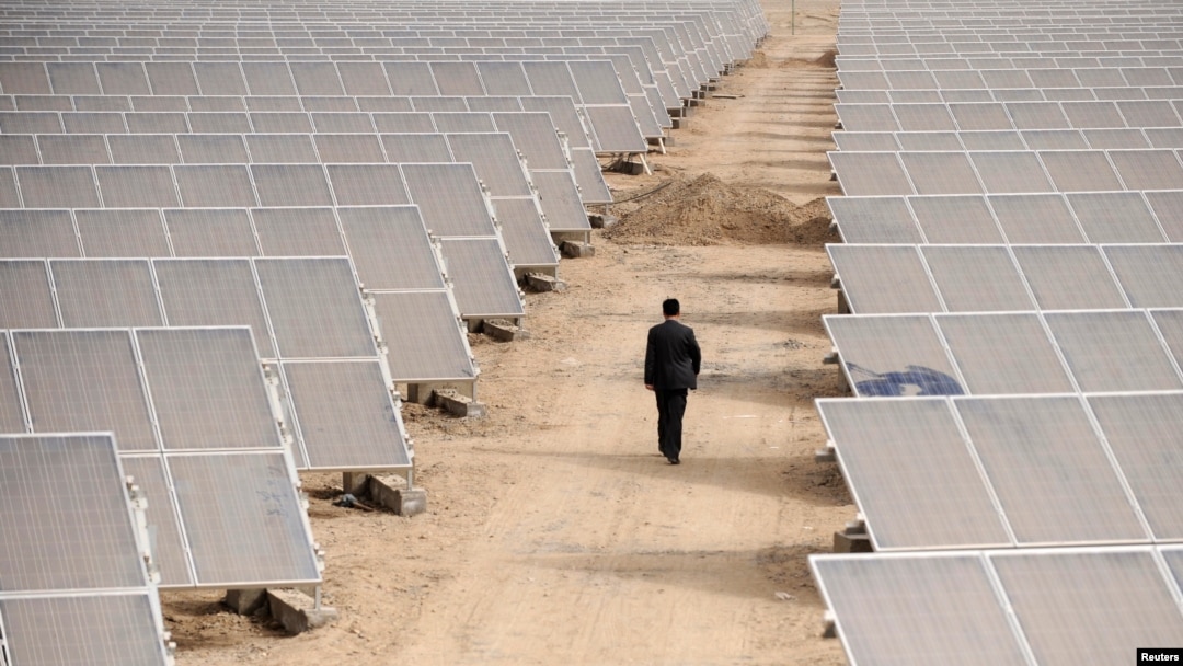 ARCHIVO - Un hombre camina a través de paneles en una planta de energía solar en Aksu, Región Autónoma Uigur de Xinjiang, 5 de abril de 2012.