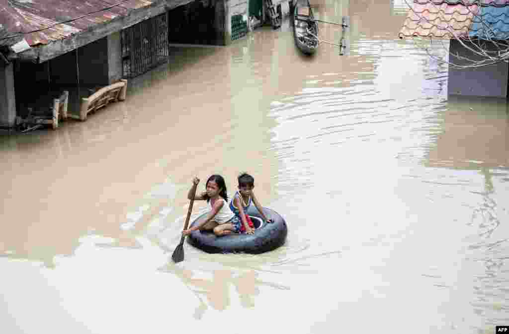 Children use a tire's interior to cross a flooded street in the aftermath of Super Typhoon Mangkhut at Salonga Compound in Calumpit, Bulacan, Philippines.