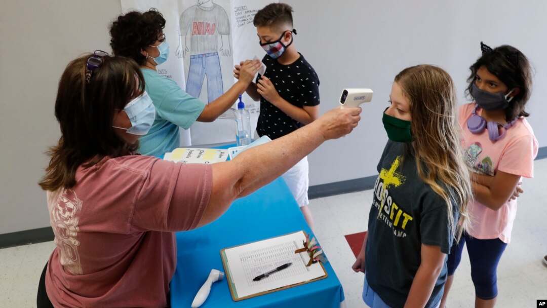FILE - In this July 14, 2020, file photo, amid concerns of the spread of COVID-19, science teachers Ann Darby, left, and Rosa Herrera check-in students before a summer STEM camp at Wylie High School in Wylie, Texas. Schools and camps across the county are