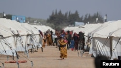 Una niña camina mientras carga a un niño frente a las tiendas de campaña erigidas para los desplazados internos después de un terremoto, en la ciudad rebelde de Jandaris, Siria, el 4 de marzo de 2023.