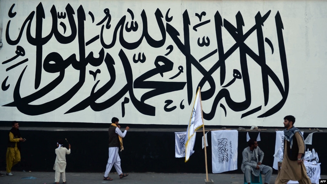 FILE - A vendor selling Taliban flags waits for customers next to a large Taliban flag in Kabul, Afghanistan, on Sept. 24, 2021. 