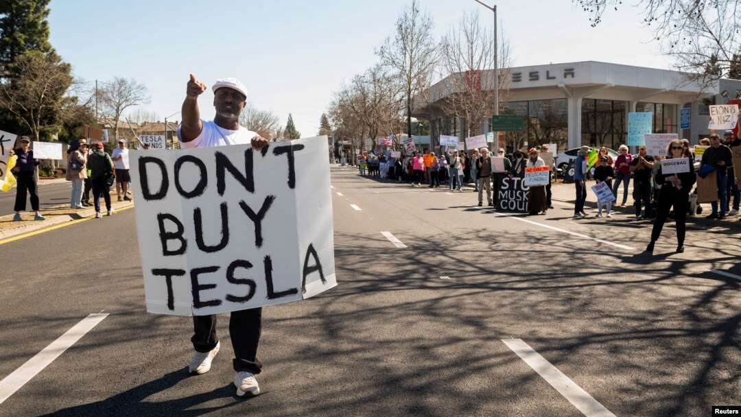People protest against Tesla and Elon Musk outside of a Tesla dealership in Palo Alto, California, on March 8, 2025. U.S. President Donald Trump said on March 11 he would buy a Tesla vehicle as a show of support as the company becomes a focal point of protests against Musk.