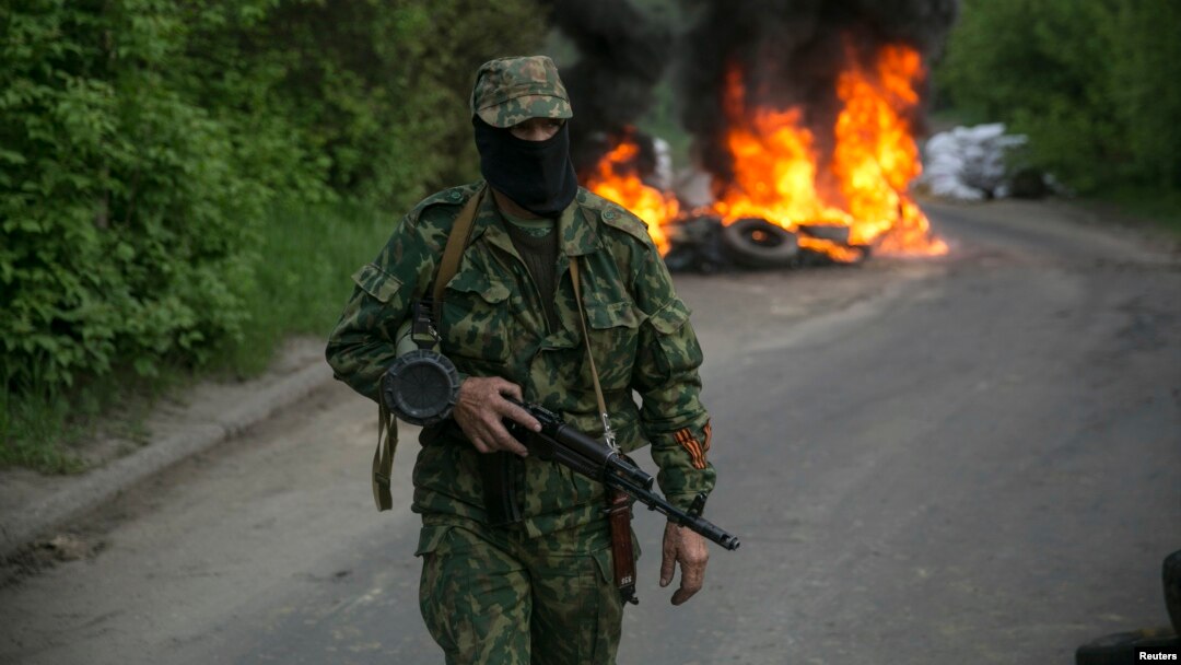 Un separatista prorruso vigilan en un retén en las afueras de Slaviansk, en Ucrania oriental. En el fondo arden unas llantas de automóvil.