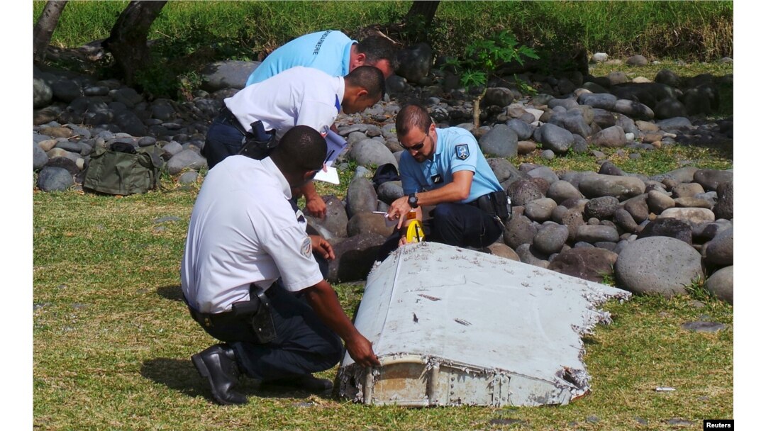 FILE - French gendarmes and police inspect a large piece of plane debris which was found on the beach in Saint-Andre, on the French Indian Ocean island of La Reunion, July 29, 2015.