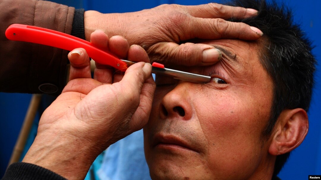 FILE - A barber uses a razor to clean the eyelids of his customer, as a part of his hair shaving service, at a residential area in Suining, Sichuan province, Feb. 23, 2012. 